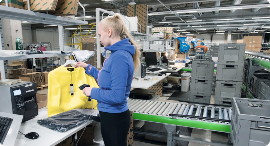 WMS integrert inne på et lager. Her står en dame å scanner varer ved hjelp av WMS shark