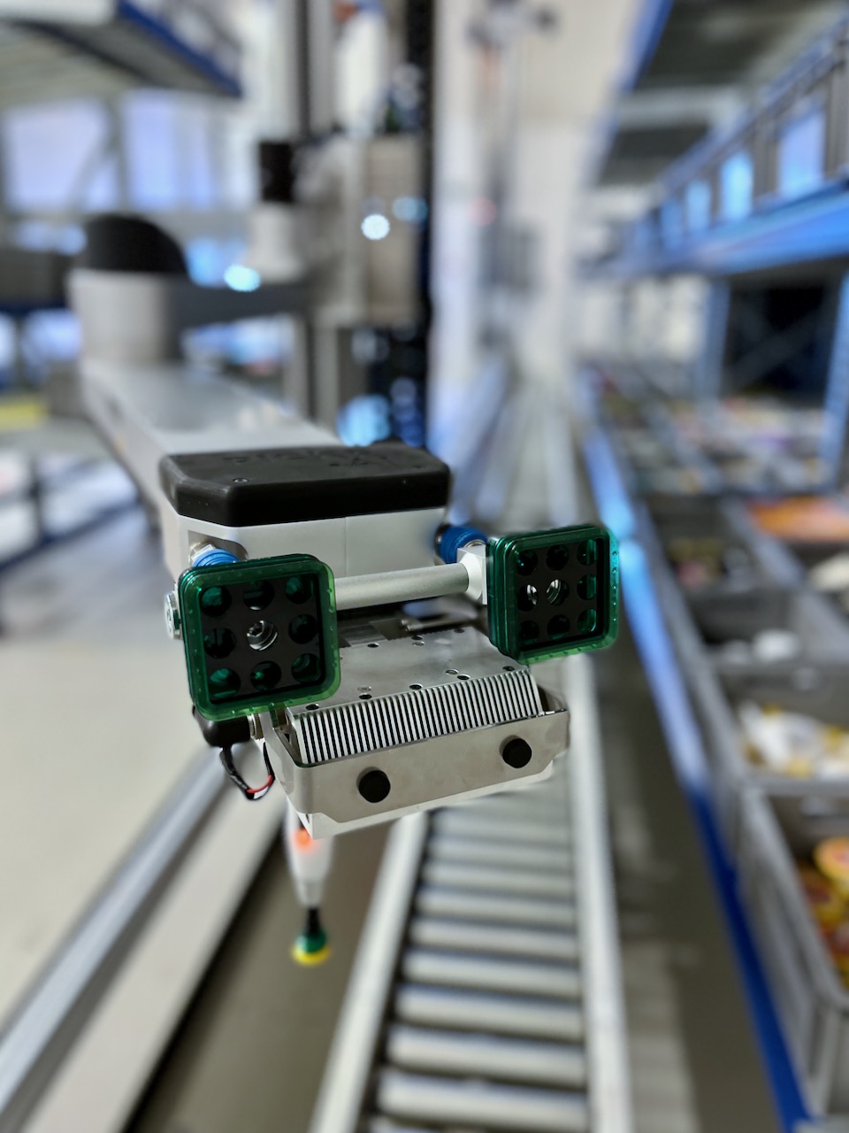 Nærbilde av plukkerobotens gripearemer i fokus, med deler av lageret uskarpe i bakgrunnen. Robotens teknologiske detaljer og dens rolle i automatisering av lageroperasjoner er tydelig fremhevet.