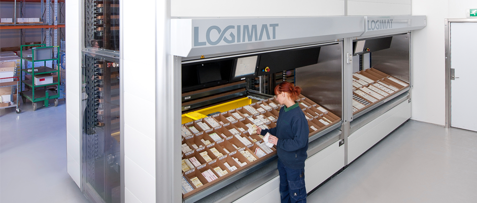 En arbeider i blå arbeidsklær velger varer fra en automatisert lagerhylle merket LogiMAT.
